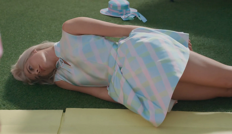 image from the Barbie movie where barbie (margot robbie) is lying on the ground looking hopeless